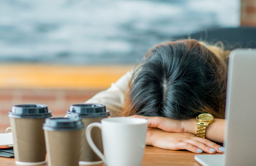 Fatigue au travail et récupération Femme épuisée au travail avec plusieurs cafés, illustrant la fatigue, le manque de récupération et l’importance d’une nutrition adaptée